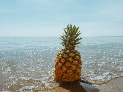 Ananas appoggiato a riva di mare fra le onde dell'oceano